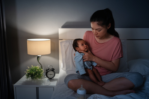 mother holding newborn baby burping after feeding milk on a bed at night