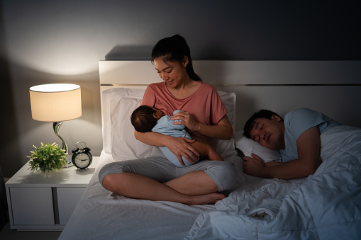 Madre amamantando a un bebé Newborm mientras su esposo duerme en la cama por la noche photo