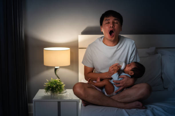 père endormi bâillant et donnant du biberon au nouveau-né au lit la nuit - baby yawning asian ethnicity newborn photos et images de collection