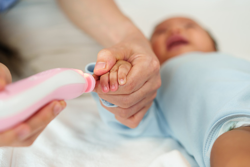 mother cutting newborn baby's fingernails with auto electic nail trimmer.