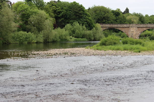 istock View across a wide shallow river to a tree lined riverbank, with an old stone arched bridge in the background 1519489400