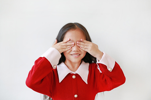 Portrait of happy little Asian child girl covering eyes with hands isolated over white background.