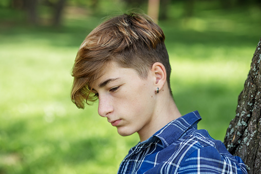 Portrait of serious teenager sitting on grass in park. Gen Z. Unhappy and stress.