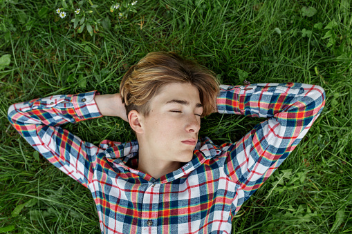 Portrait of serious teenager who lies in grass and rests. Gen Z. Identity development. Sleep.