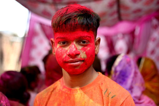 Happy teenage boy of Indian ethnicity celebrating Holi festival and his face painted with powder paint. Holi is a popular and significant Hindu festival celebrated as the Festival of Colours, Love and Spring. It celebrates the eternal and divine love of the god Radha and Krishna.