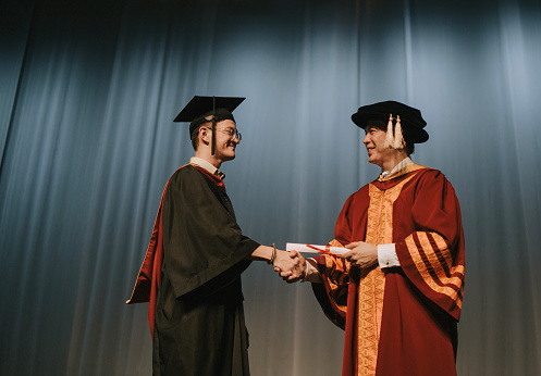 Convocation ceremony Asian Graduation university student handshake with Dean on Auditorium stage receiving certificate