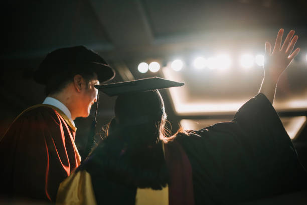 istock Convocation ceremony Excited Asian Graduation university female student arm raised standing beside Dean after received Graduation Scroll on Auditorium stage 1519543069