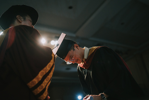 Asian Dean performing the turning of the tassel for university student during convocation ceremony on stage, flip the tassel from one side of the cap to another and this signifies the earning of a degree