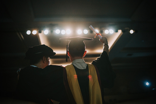 Convocation ceremony Excited Asian Graduation university student arm raised standing beside Dean after received Graduation Scroll on Auditorium stage