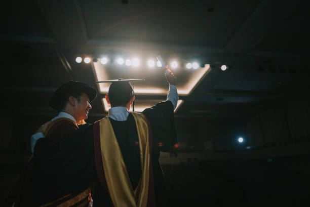 istock Convocation ceremony Excited Asian Graduation university student arm raised standing beside Dean after received Graduation Scroll on Auditorium stage 1519543722