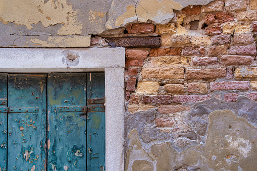 Detail with a green wooden shutter window on a worn out plastered red brick wall, in Venice Italy.