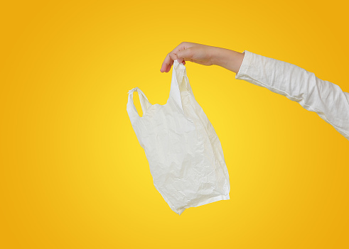 Closeup children hand holding a white thin polythene plastic bag isolated on yellow background.