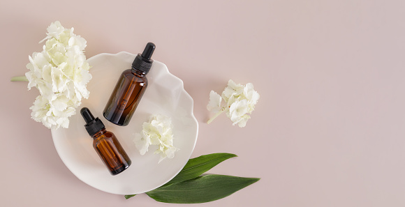 Top view of two cosmetic bottles with a dropper with a natural product for additional self-care on a white abstract plate. banner