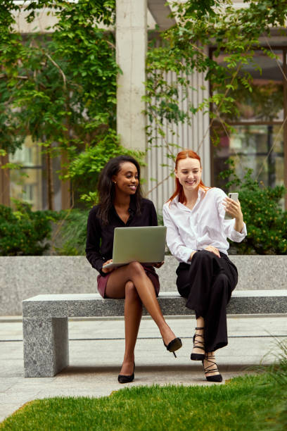 istock Smiling, positive office workers, stylish women sitting outside office, working and having online video call 1519559369
