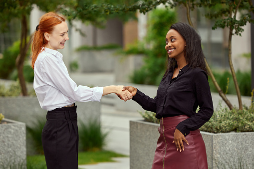 Future cooperation and partnership. Two women, employees standing outside and shaking hands. Successful teamwork. Concept of business, career development, modern office, professional occupation
