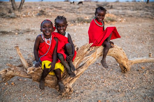 Three happy African little girls from Samburu tribe sitting on tree trunk, Kenya, Africa. Samburu tribe is north-central Kenya, and they are related to  the Maasai.