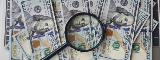 istock Magnifying glass and dollar bills on laptop closeup 1519592572