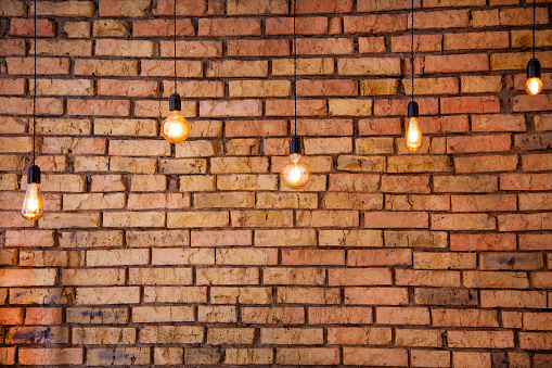 Old electric incandescent lamps with tungsten filament. Against the backdrop of a brick wall. Texture of old stone background. Decorative vintage design edison lightbulbs of different shapes. Antique