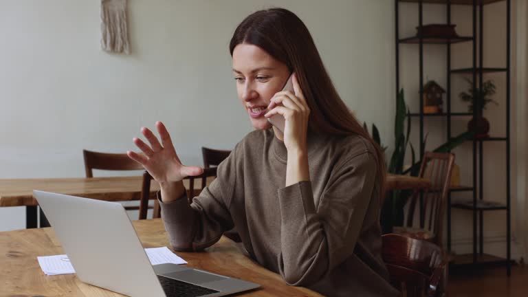 Businesswoman sitting at desk with laptop enjoy conversation on cellphone