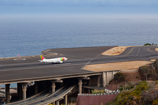 Funchal, Madeira, Portugal, Europe- June 20,2023: Airbus from TAP Portugal approaching the runway of Madeira Airport  LPMA,  also known as Funchal Airport and Santa Catarina Airport,  next to a busy highway,  Santa Catarina