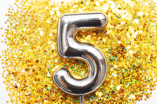 Five years birthday party. Festive silver big number five with golden confetti in the form of stars on a yellow background. Holiday celebrate and anniversary concept.