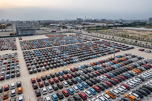 Many new cars are parked in large parking lots on the international cargo terminal