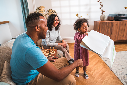 Embracing happiness and cheer at home, a cute small mixed-race girl showcases her artistic talent through coloring, bringing smiles to her delighted father and grandmother as they admire her drawings.