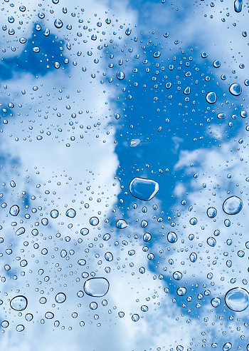 Overhead view of clear raindrops at transparent window glass surface on a sunny day with cloud blue sky, selective focus. Abstract purity background. Freeform pattern by nature.