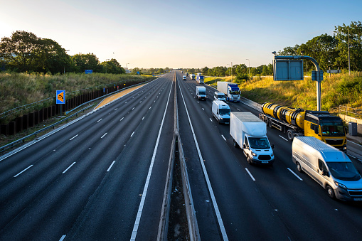 heavy truck traffic moving at speed on uk motorway in england at sunrise with one line empty.