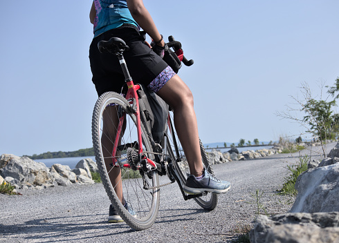 burlington, vt - june 15, 2023: woman riding bike on gravel trail (young south asian, indian rider on bicycle trail) burlington vermont causeway path (brown skin, athletic clothes, cycling jersey, helmet)