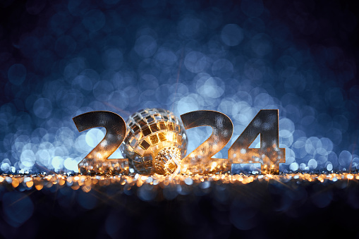 Abstract Christmas / New Year 2024 background. Metallic numbers and a disco ball Christmas ornament on shiny stars, glitter and defocused lights in a yellow blue contrast. Native image size: 7952x5304