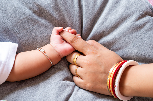 Infant baby holding mother's index finger. Lovely, emotional, sentimental moment. Trust and care concept. Closeup. Top down view.