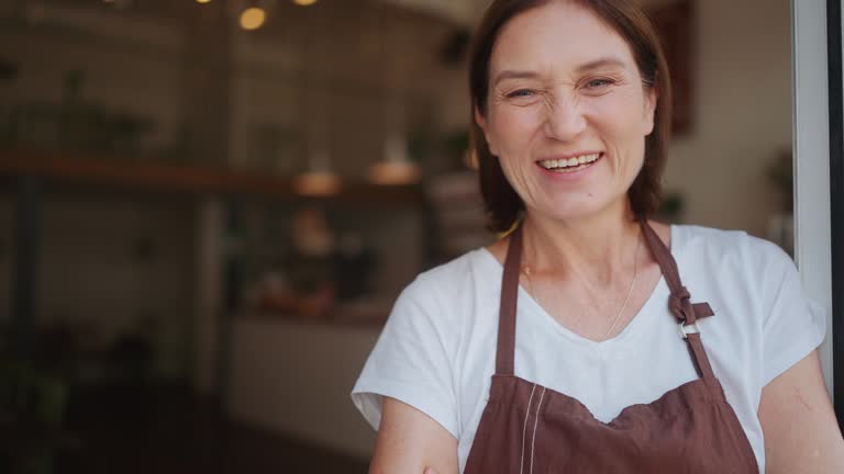 Close-up view of cheerful old barista looking at camera at entrance