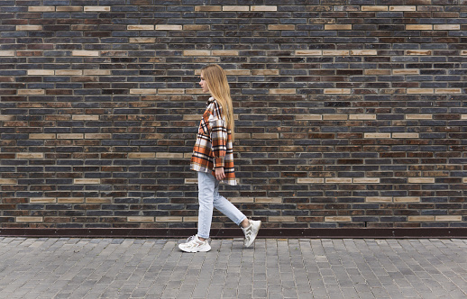 young woman walks down the street in front of a brick wall