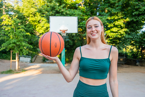 A smiling girl with a basketball in a basketball court ready to play.