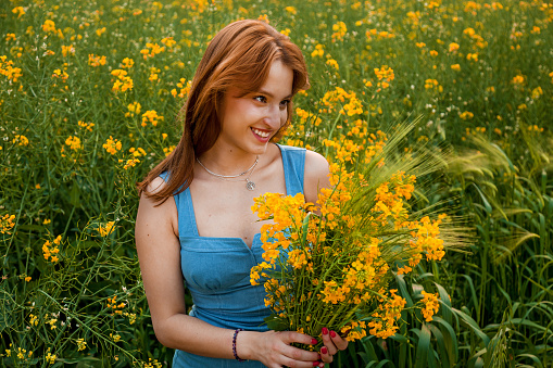 The girl holds in her hands a bouquet of yellow rapeseed flowers and green spikelets of wheat on the field