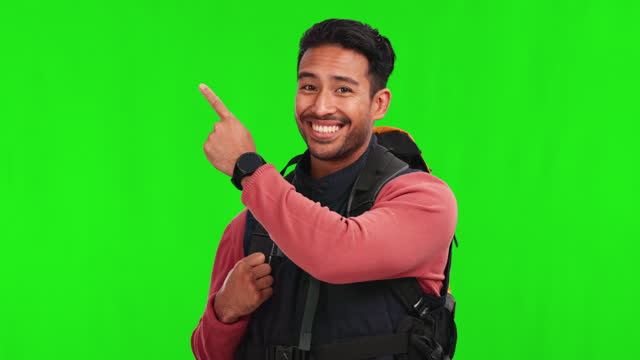 Asian man, hiker and pointing on green screen for list or travel against a studio background. Portrait of happy male person or traveler backpack show notification for advertising on mockup space