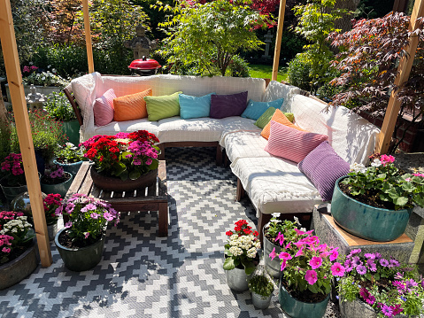 Stock photo showing ornamental Japanese-style garden with outdoor lounge area in Summer. Featuring a large expanse of white, interconnecting, white plastic decking tiles with outdoor patterned rug, providing a family space for outdoor hardwood, cushion covered seating.