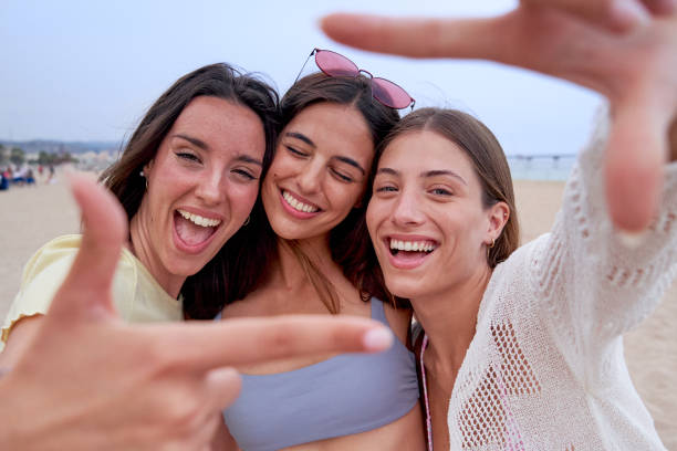 istock Happy female friends on beach together, looking at camera smiling and gesturing a frame with fingers 1520061241