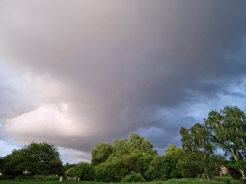View of dark storm clouds rolling in over green trees and grass fields