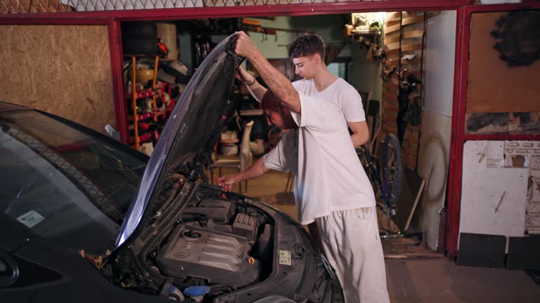 Teenage boy assist to his father, while he repairing the car, in the messy garage