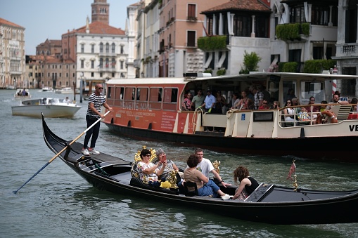 (IPTC format photo metadata added to file for press use) Gondoliers riding their gondolas in old city of Venice island to transport tourists between locations in summer. Private riding with a gondola starts from 80 Eur for 25 minutes in its season. There are only around 250 gondolas on service for tourists today.