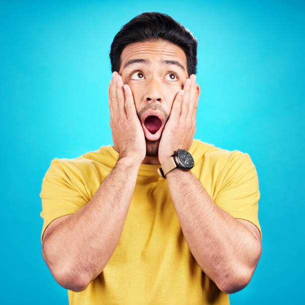 istock Wow, shocked and man with hands on face and mouth open for surprise or announcement in studio. Male model person on a blue background while thinking of gossip, sale or promotion with comic emoji 1520182014