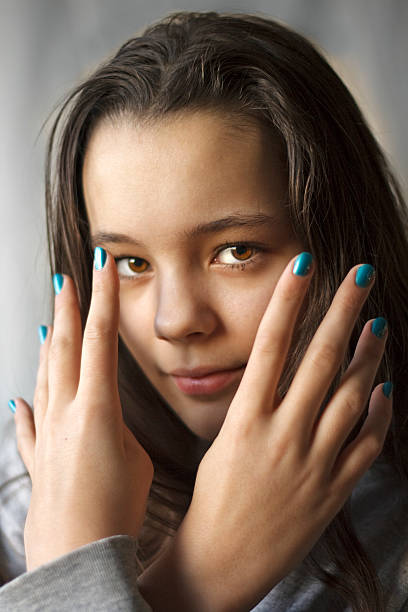 Girl with brown eyes and hands with manicured fingers on grey background.