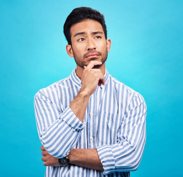 istock Thinking, planning and future with a man on a blue background in studio to consider a thought or option. Idea, mindset and contemplation with a handsome young person looking thoughtful about a choice 1520191449