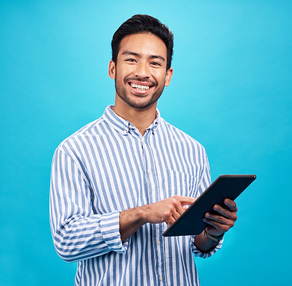 Tablet, man portrait and smile in a studio on social media, internet and website app scroll. Happiness, isolated, and blue background with a male model reading a ebook for digital networking
