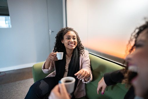 Friends businesswomen talking while holding a mug of coffee at office