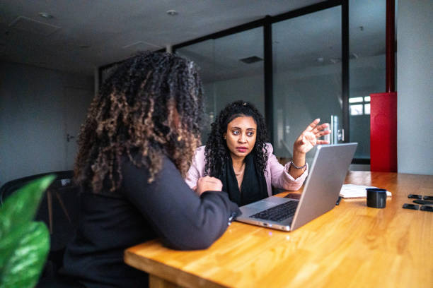 istock Businesswoman talking/explaining to her coworker while using laptop at office 1520210890