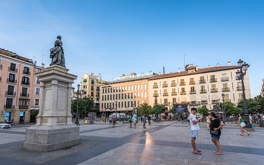 Madrid, Spain - June 26, 2023: Tourists walking in front of the Royal Theater (Teatro Real) at sunset, situated at the Plaza de Oriente (Orient Square), in Madrid. The Plaza de Isabel II (Plaza de Ópera) is a historic public square between the Sol and Palacio wards in the central district of Madrid.