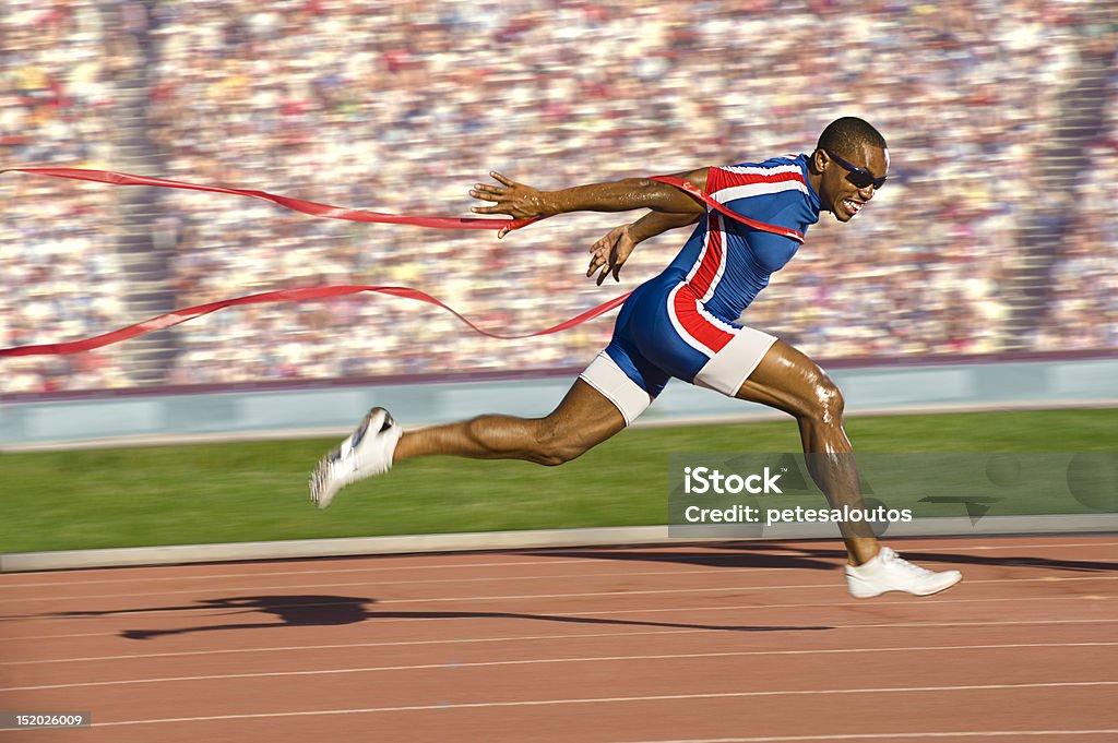 Sprinter Crossing the Finish Line African-American sprinter crossing the finish line and breaking the tape. Horizontally framed shot. Running Stock Photo